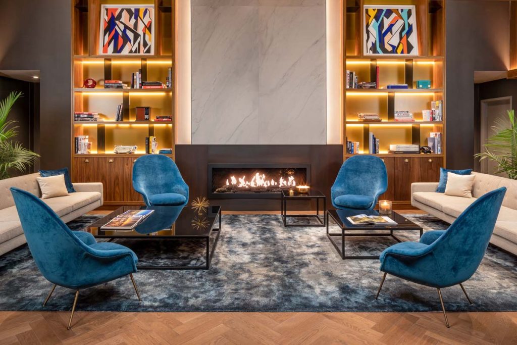 Cozy hotel lounge with roaring fire, teal velvet chairs, and tall wood bookcases