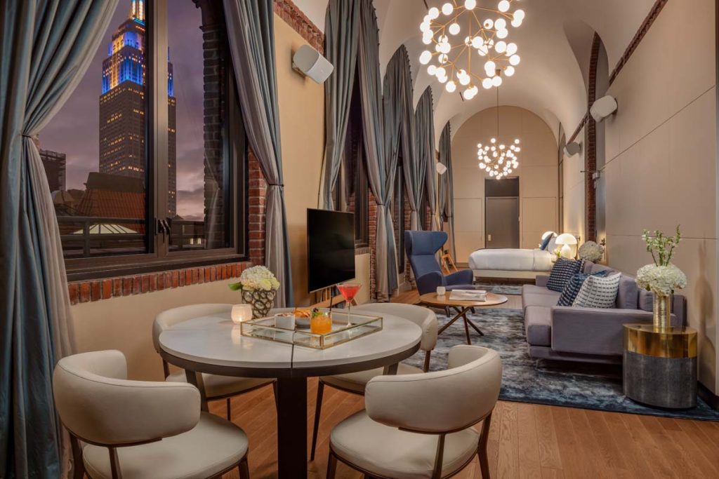 Large hotel suite with cozy bed, warm lighting, and a seating area with table and upholstered chairs